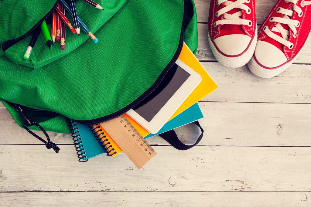 Green backpack with school supplies on wooden floor